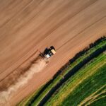 Aerial view of a tractor ploughing a brown field next to a green pasture.