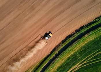 Aerial view of a tractor ploughing a brown field next to a green pasture.